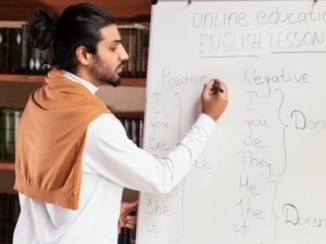 Indian Teacher Teaching English Distantly Writing On Blackboard Standing Indoors