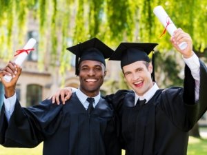 Graduated together. Two happy young men in graduation gowns holding diplomas and rising arms up