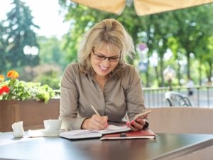 Business beautiful woman writing in business notebook using smartphone