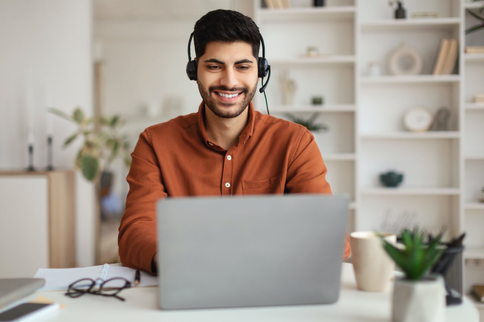 Arab man using laptop wearing headset sitting at desk