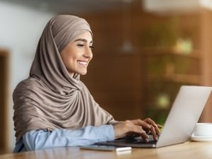 Happy arab woman chatting with clients on laptop