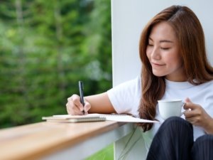 A beautiful young asian woman writing on a notebook in the outdoors
