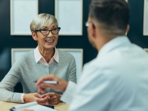 Smiling senior woman patient in doctor's office counseling a male doctor