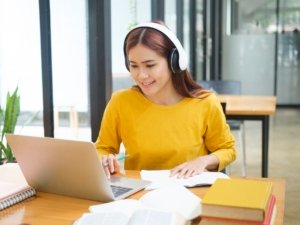 Woman learning online using laptop and writing notes.