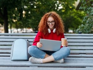 Happy female student enjoying coffee and using laptop