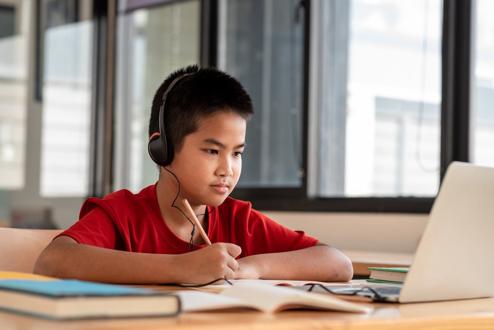 Image of a male student studying online wearing headphones and taking notes on his laptop placed in