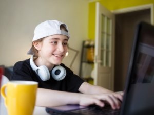 teen child is sitting at home at laptop and playing computer games.