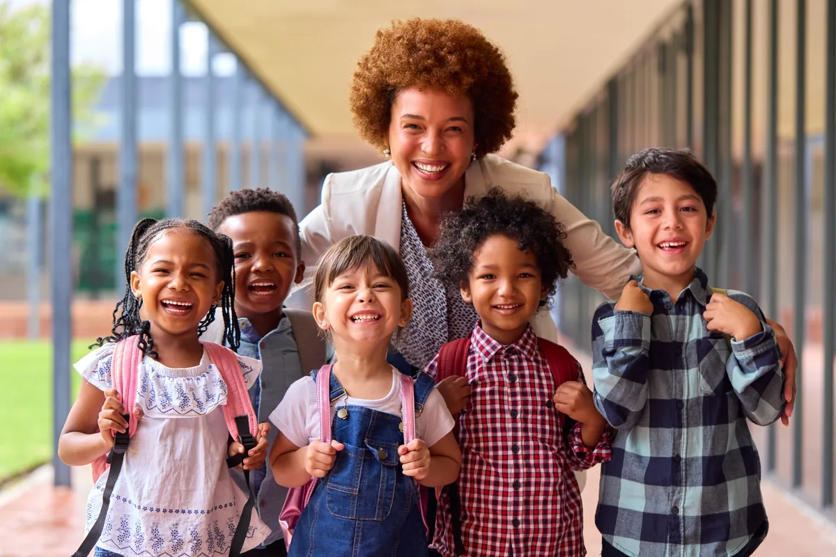 Smiling teacher standing with a group of pupils in a bright school corridor.