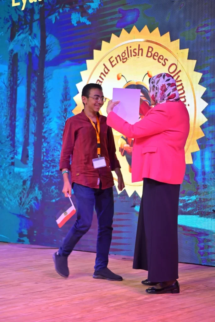 Presenter giving an award to a participant on a stage with WEB Olympiad branding.