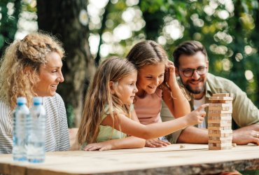 Family is sitting at the table in nature and playing jenga game.