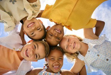 Group Of Multi-Cultural Children Friends Linking Arms Looking Down Into Camera