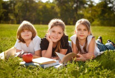 happy little school kids with notebooks laying in outdoor park. group portrait looking at camera