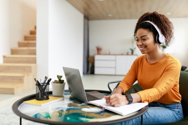 Woman sitting at desk, using computer and writing in notebook